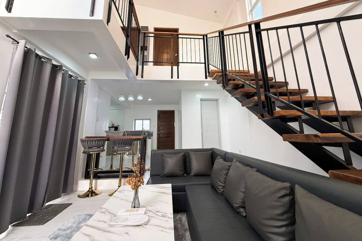 A modern living room with a sofa, a dining area, and a staircase.