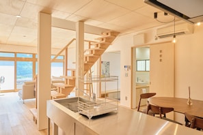 A modern kitchen with a wooden staircase, a dining area with a round table, and a view of the outside.