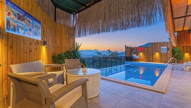 Zona de piscina con mobiliario de mimbre, piscina de cristal y vistas a las montañas.