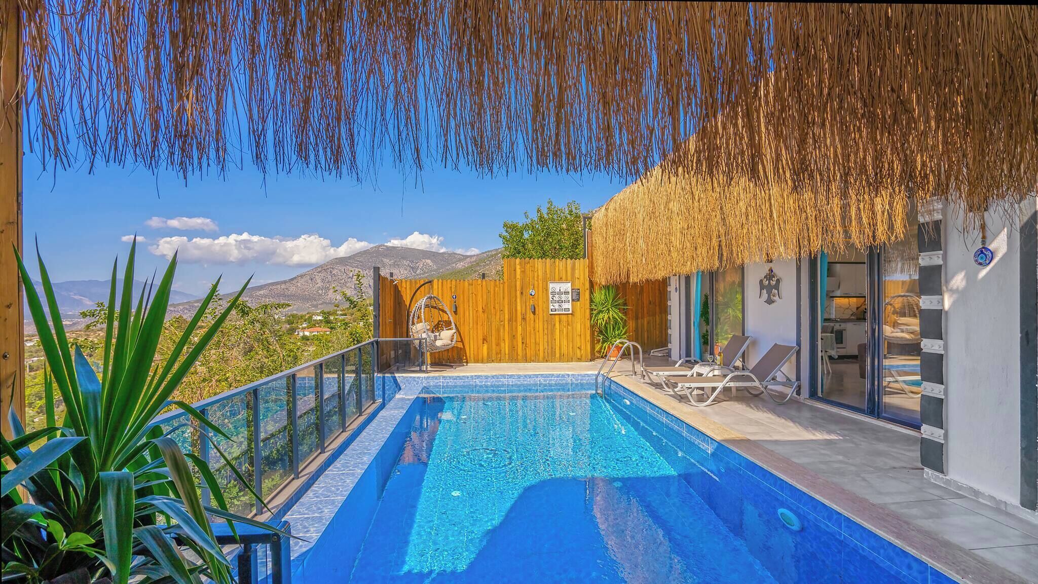 A pool with a wooden deck, a thatched roof, and a view of mountains.