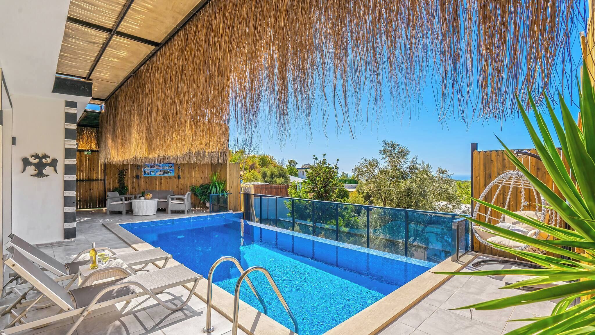 Une piscine dotée d’une paroi en verre, de chaises longues et d’une structure à toit de chaume.