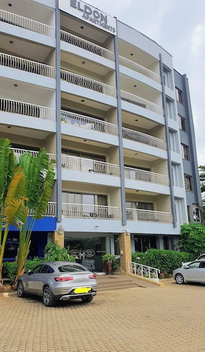 Un immeuble à plusieurs étages doté de balcons, une enseigne indiquant « Eldon Apartments », et des voitures garées devant.
