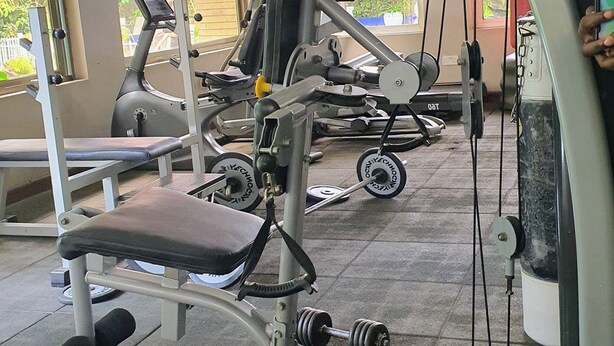 Et fitnesscenter med forskellig træningsudstyr, store vinduer og udsigt til bygninger.
