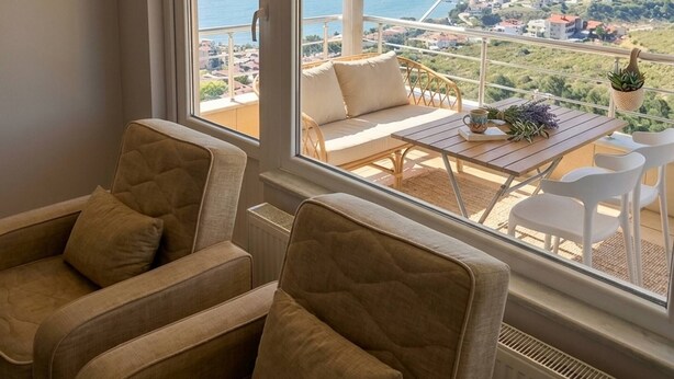 A room with a large window overlooking a coastal view, a seating area with a table, and a hanging light fixture. - Quiet and Comfortable in Sinop Karakum Site 2 (Sinop Merkez)