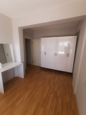 Una habitación con un armario blanco, un escritorio blanco y suelo de madera.