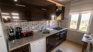 A modern kitchen with dark wood cabinets, a granite countertop, a built-in dishwasher, and a window with a view of greenery. - Quiet and Comfortable in Sinop Karakum Site 2 (Sinop Merkez)
