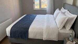Ein Hotelzimmer mit Bett, Fenster mit Blick, Heizkörper und Nachttisch mit Flasche und Glas.