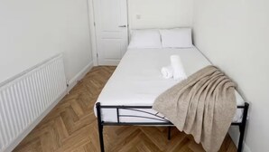 A single-bed room with a white mattress, a beige blanket, and a white door. - Gladeside Luxe Three Bed Retreat (Croydon)