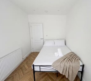 A single-bed room with a white mattress, a beige blanket, and a white door. - Gladeside Luxe Three Bed Retreat (Croydon)