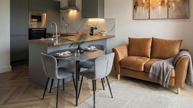 A modern kitchen with a built-in oven, a dining area with a table and chairs, and a living area with a sofa and artwork on the wall. - Gladeside Luxe Three Bed Retreat (Croydon)