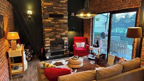 A cozy living room with a stone fireplace, a red armchair, a sofa, and a large window overlooking a deck.