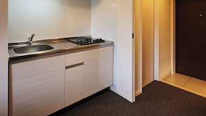 A compact kitchen with a sink, stove, and cabinets, leading to a door. - Residence Hotel Hakata Station2 (Fukuoka)