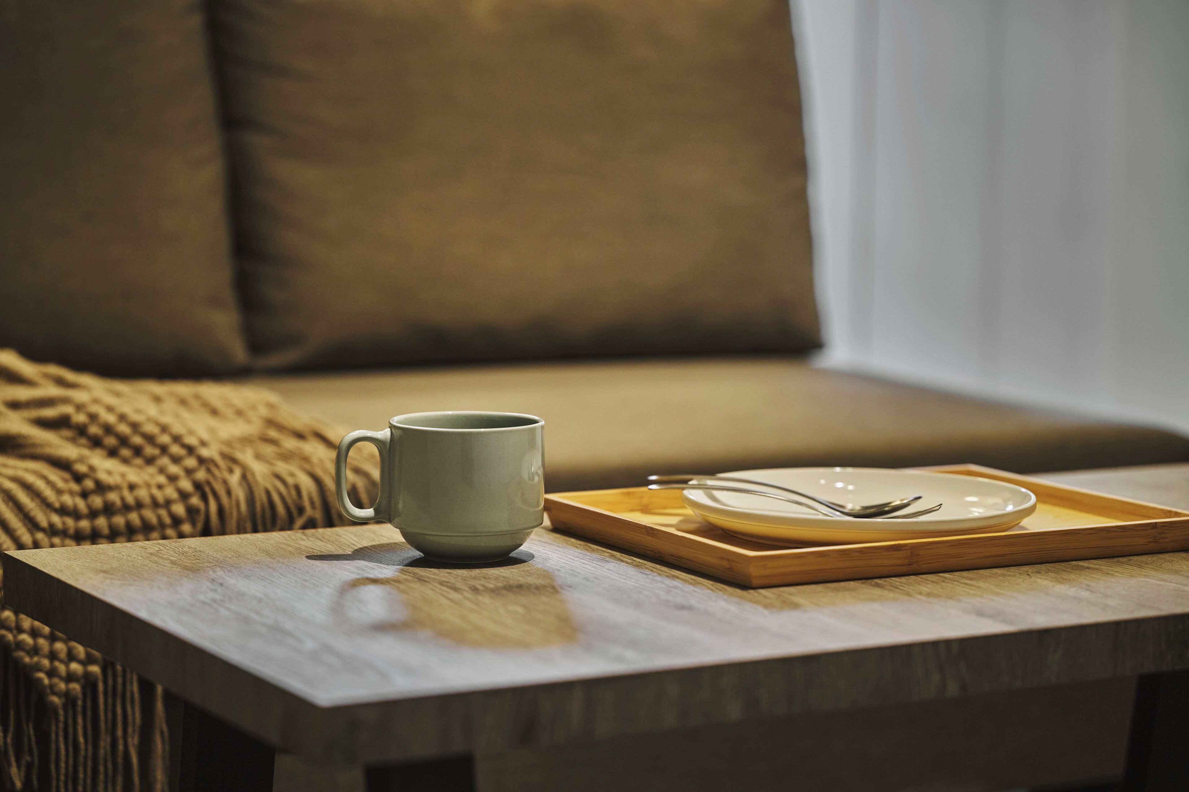 Une table en bois sur laquelle se trouvent une tasse en céramique et une assiette avec des couverts.