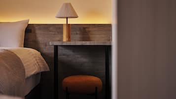 Una camera d'albergo con un letto, un comodino, una lampada e uno sgabello.