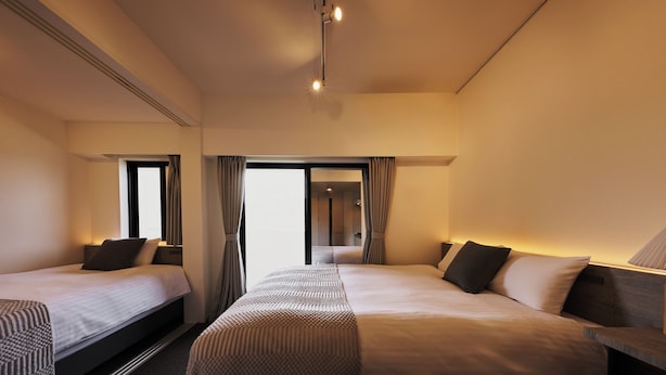 A hotel room with two beds, a bedside table with a lamp, a window with curtains, and a door leading to another room. - Residence Hotel Hakata Station2 (Fukuoka)