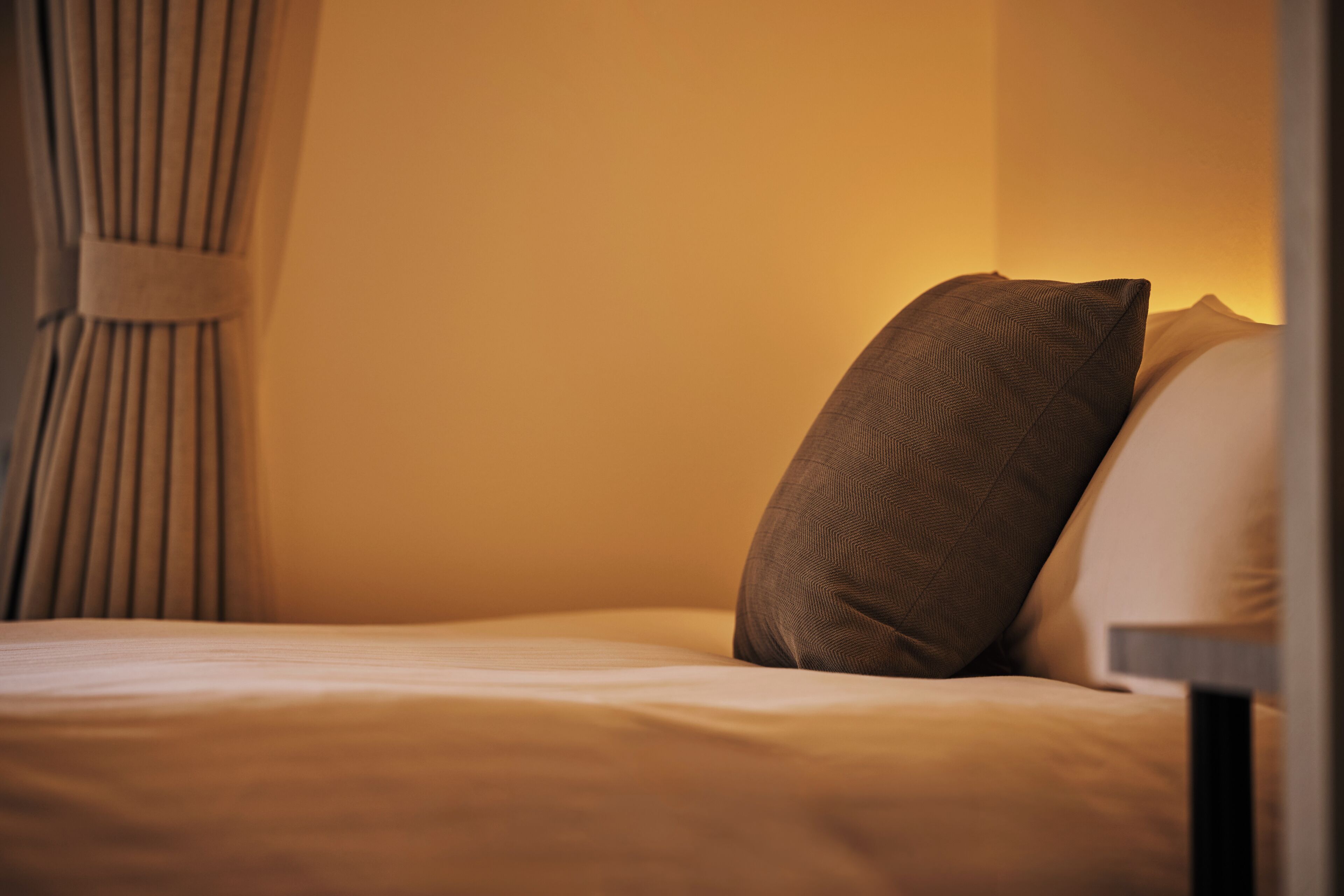 A neatly made bed with pillows, a headboard, and a curtain.