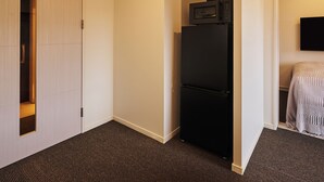 A hotel room with a black refrigerator, a microwave on top, a bed with a striped blanket, and a TV mounted on the wall. - Residence Hotel Hakata Station2 (Fukuoka)