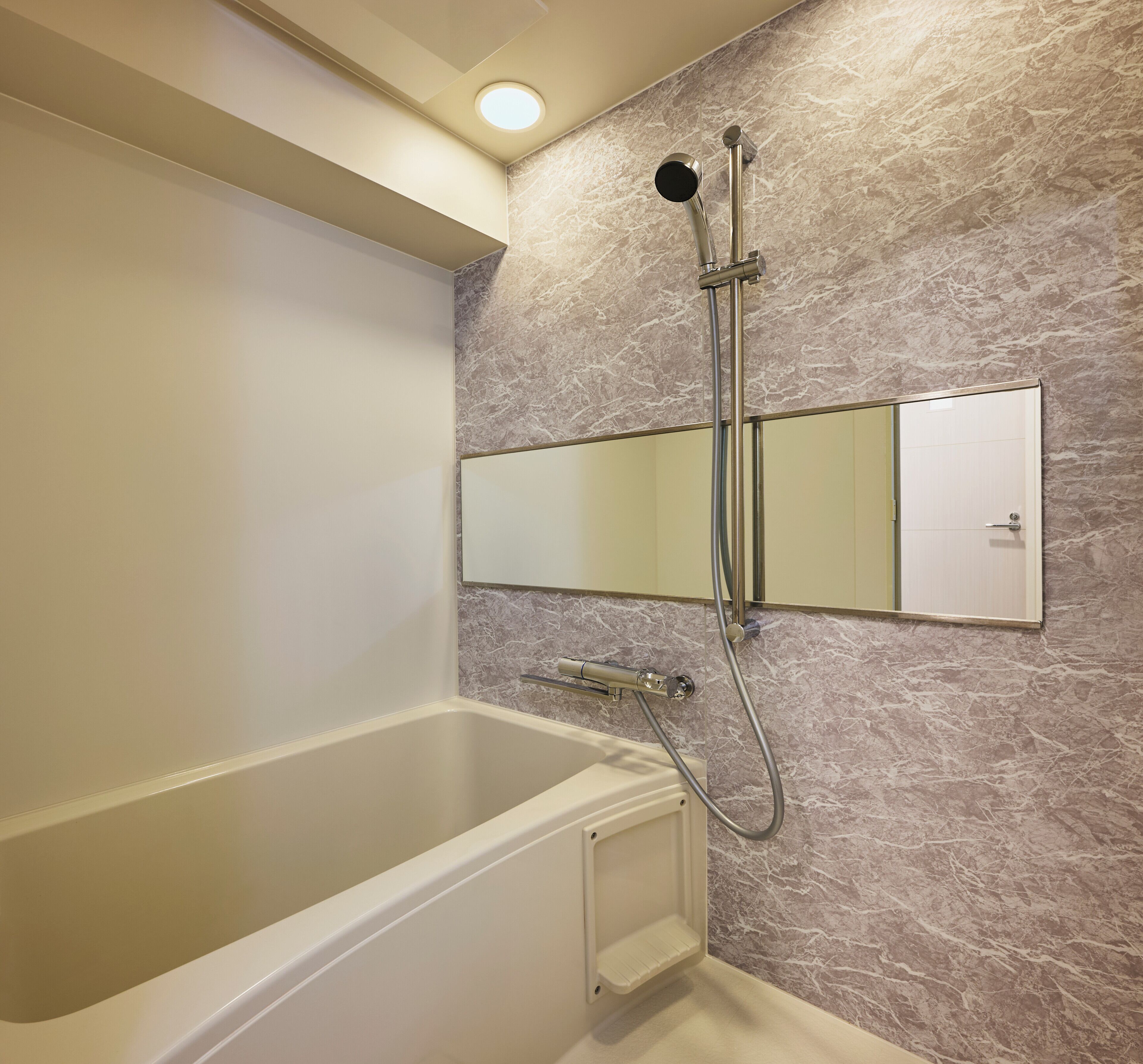 Une salle de bain équipée d’une baignoire, d’une douche, d’un miroir fixé au mur et d’un mur à l’aspect marbré.
