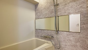 Une salle de bain équipée d’une baignoire, d’une douche, d’un miroir fixé au mur et d’un mur à l’aspect marbré.
