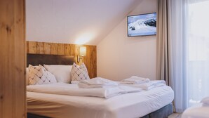 A neatly made bed with white linens, a wooden headboard, and a wall-mounted TV displaying a snowy landscape.
