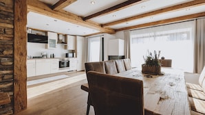 A spacious dining area with a wooden table and leather chairs, a kitchen in the background, and a stone wall on one side.