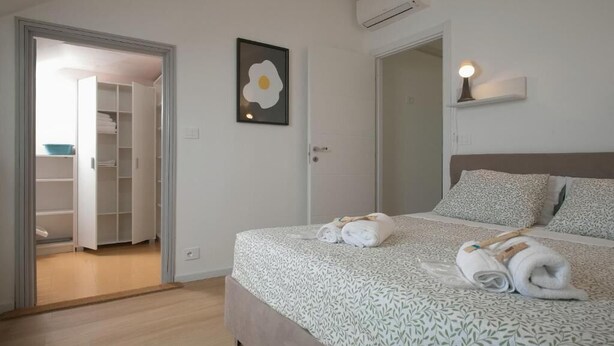A bedroom with a bed, a door, a wall-mounted light, and a framed picture. - Piccolo Attico - Wi-Fi (Turin)