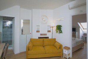 En moderne stue med sofa, lille sofabord, lampe, seng og et glasvæg bruseområde.