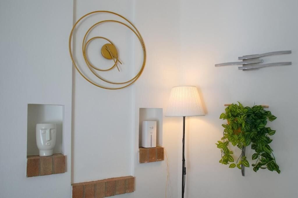 En væg med en gylden cirkeldekoration, en hvid lampe, en plante og en lille hylde med en hvid genstand.