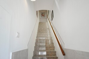 Un escalier avec une rampe, des murs blancs et un tableau encadré en haut.