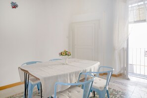 Un coin repas avec une table ronde, des chaises bleues, une nappe blanche et un vase rempli de fleurs.