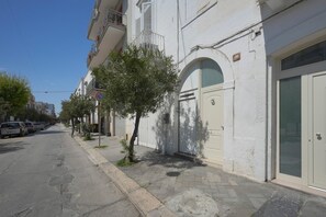 Straßenansicht mit parkenden Autos, einem Bürgersteig und einem Gebäude mit weißer Fassade und einer Tür mit Fensterteil.