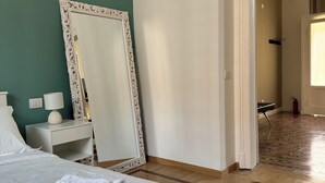 Hotellihuone, jossa on sänky, suuri peili, yöpöytä lampun kanssa ja puulattia.