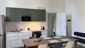 Moderni keittiö, jossa on valkoiset kaapit, sisäänrakennettu uuni ja mikroaaltouuni. Keittiössä on ruokapöytä tuoleineen ja penkkeineen.