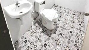 Ein Badezimmer mit Toilette, Bidet und Waschbecken, Fliesenboden mit geometrischem Muster und weißer Decke.