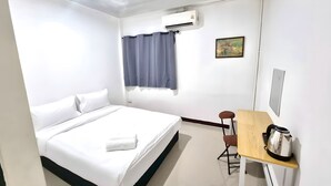 Ein Hotelzimmer mit Bett, Schreibtisch mit Wasserkocher, Fenster mit Vorhängen, Klimaanlage und einem Bild an der Wand.