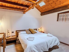 Ein Schlafzimmer mit Holzboden, einem Bett mit weißer Bettwäsche, einem Nachttisch mit Lampe und einem Fenster mit gemusterten Vorhängen.