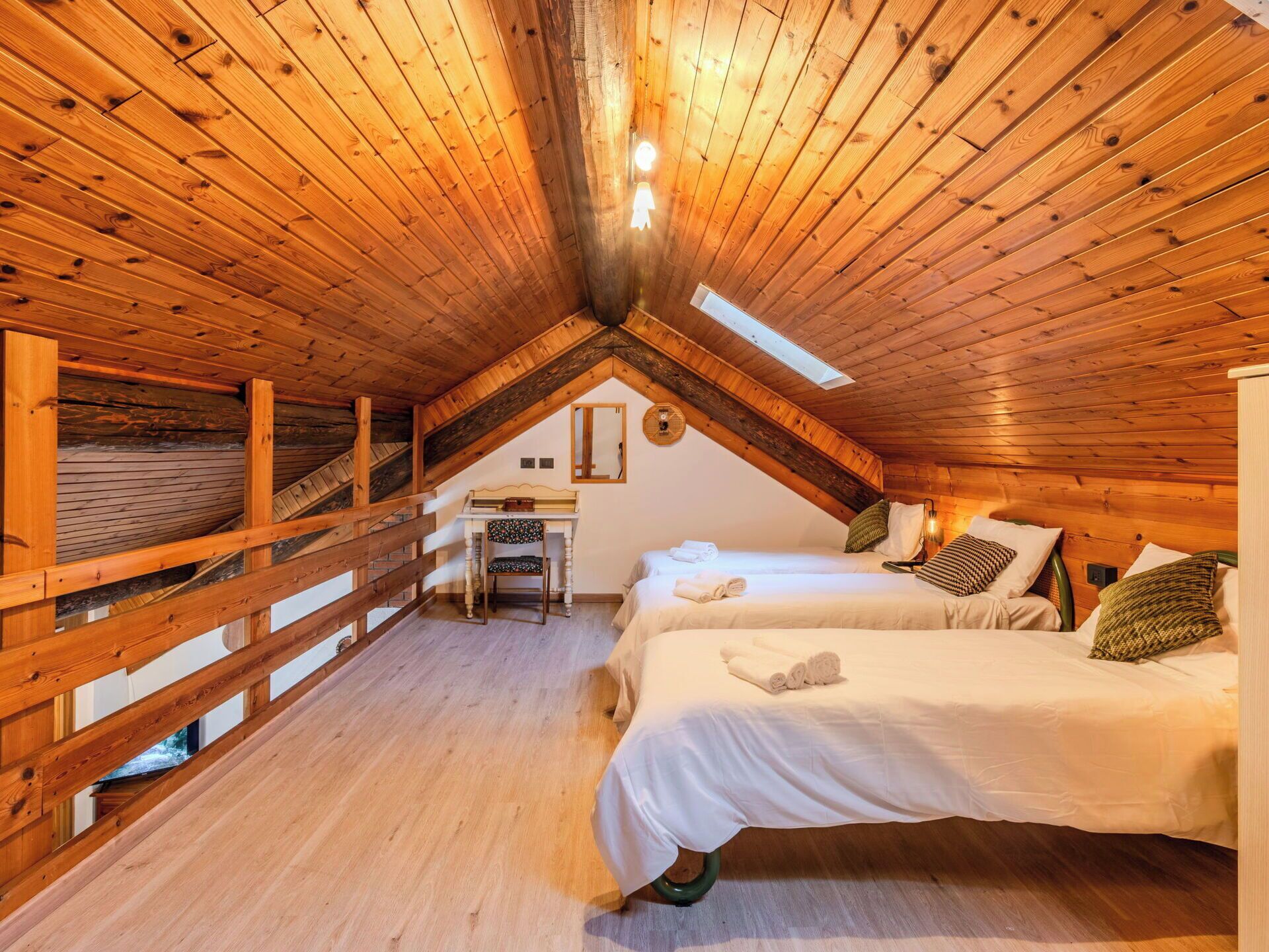 A cozy attic bedroom with wooden beams, a desk, and two beds.