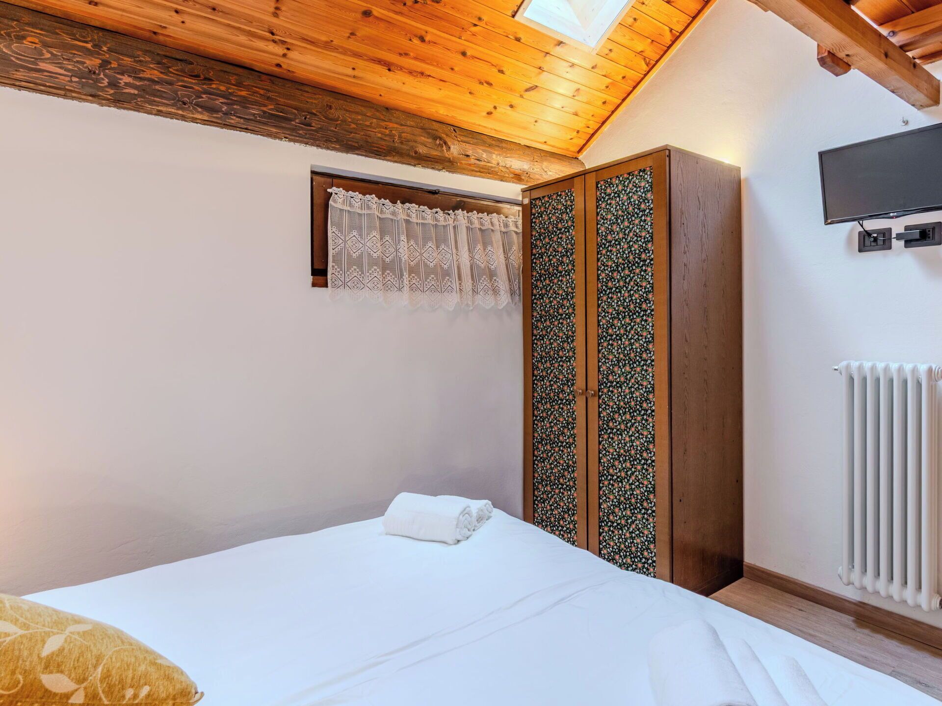 A bedroom with a bed, a wardrobe, a television, and a radiator.