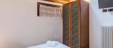 A bedroom with a bed, a wardrobe, a television, and a radiator.