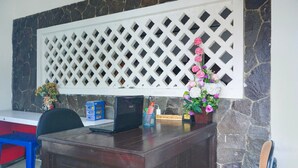 A reception desk with a laptop, a blue plastic stool, a potted plant with flowers, and a stone wall. - Luxury Deluxe DBL Retreat W/ Free WiFi and Parking (Bandar Lampung)