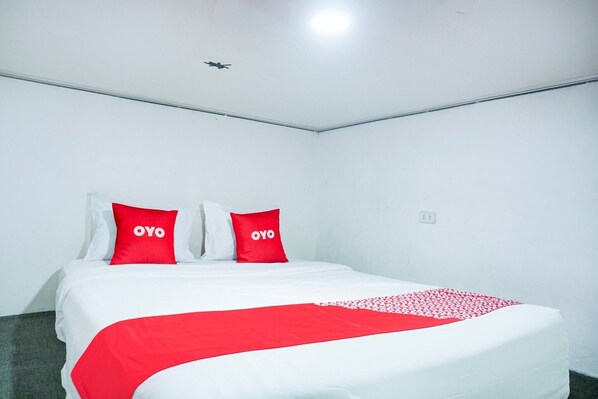 A hotel room with a bed, two red pillows with 'OYO' text, a white bedspread, and a red blanket.