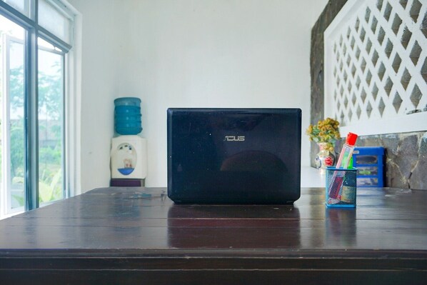 A laptop on a wooden table with a water dispenser, a small vase with flowers, and a metal container with pens and pencils.