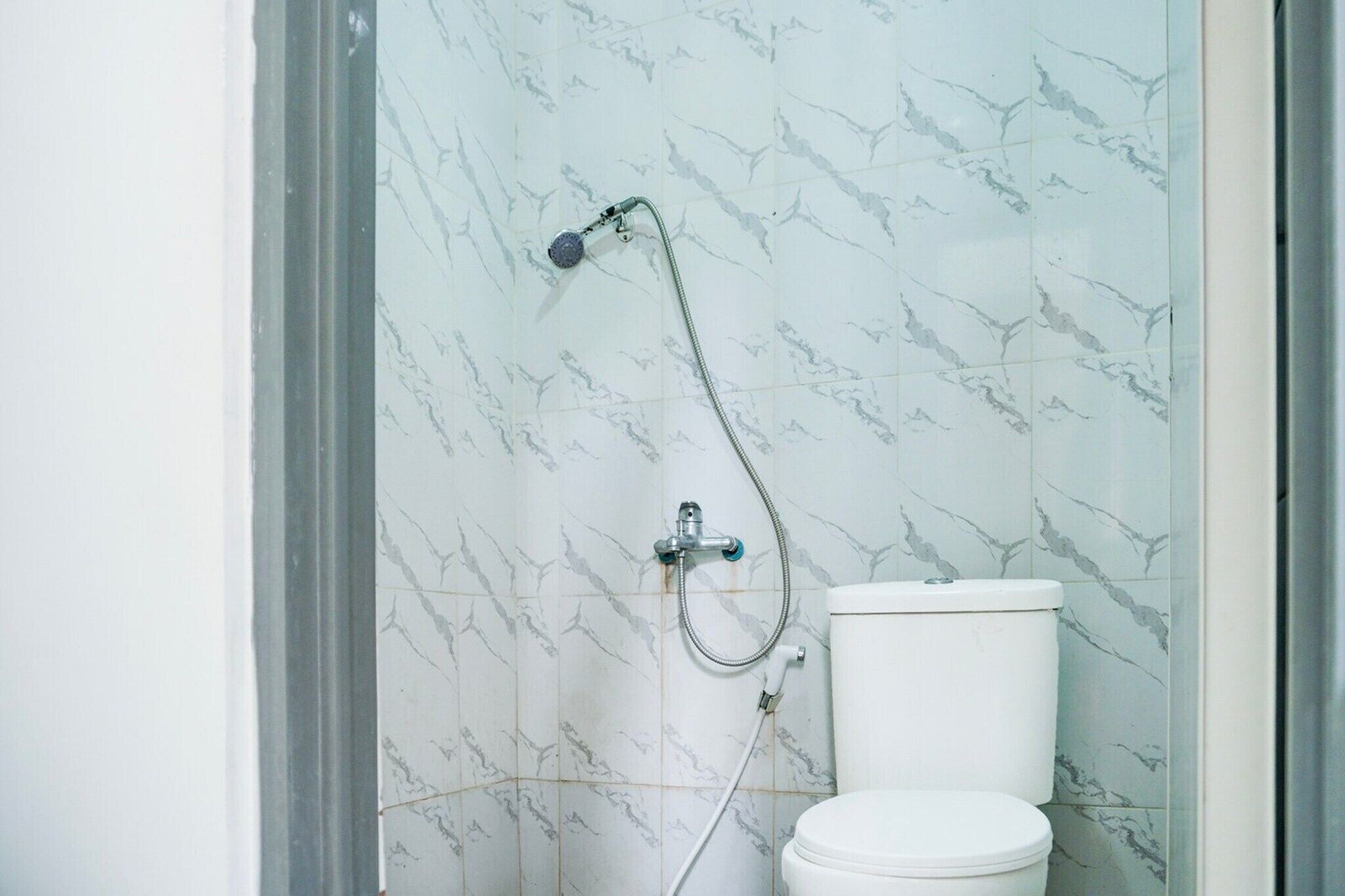 A bathroom with a toilet, a shower, and a marble-patterned wall.