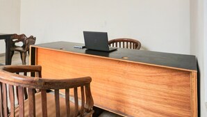 A wooden desk with a laptop, two wooden chairs, and a plain white wall.