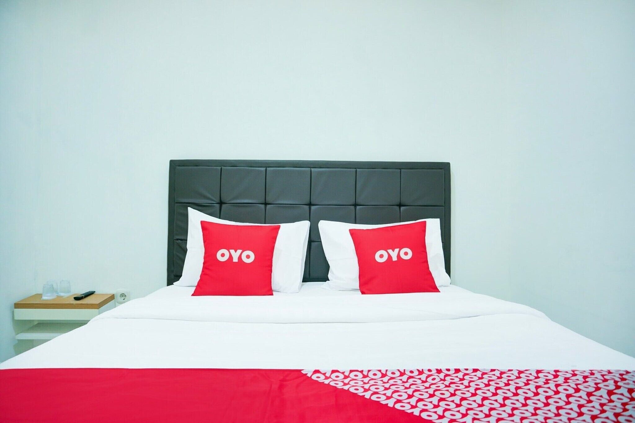 A bed with a dark headboard, two pillows with 'OYO' text, a white bedspread, and a red and white patterned blanket.