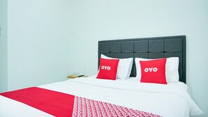 A hotel room with a bed, two red pillows with 'OYO' text, a white bedspread, and a red blanket.