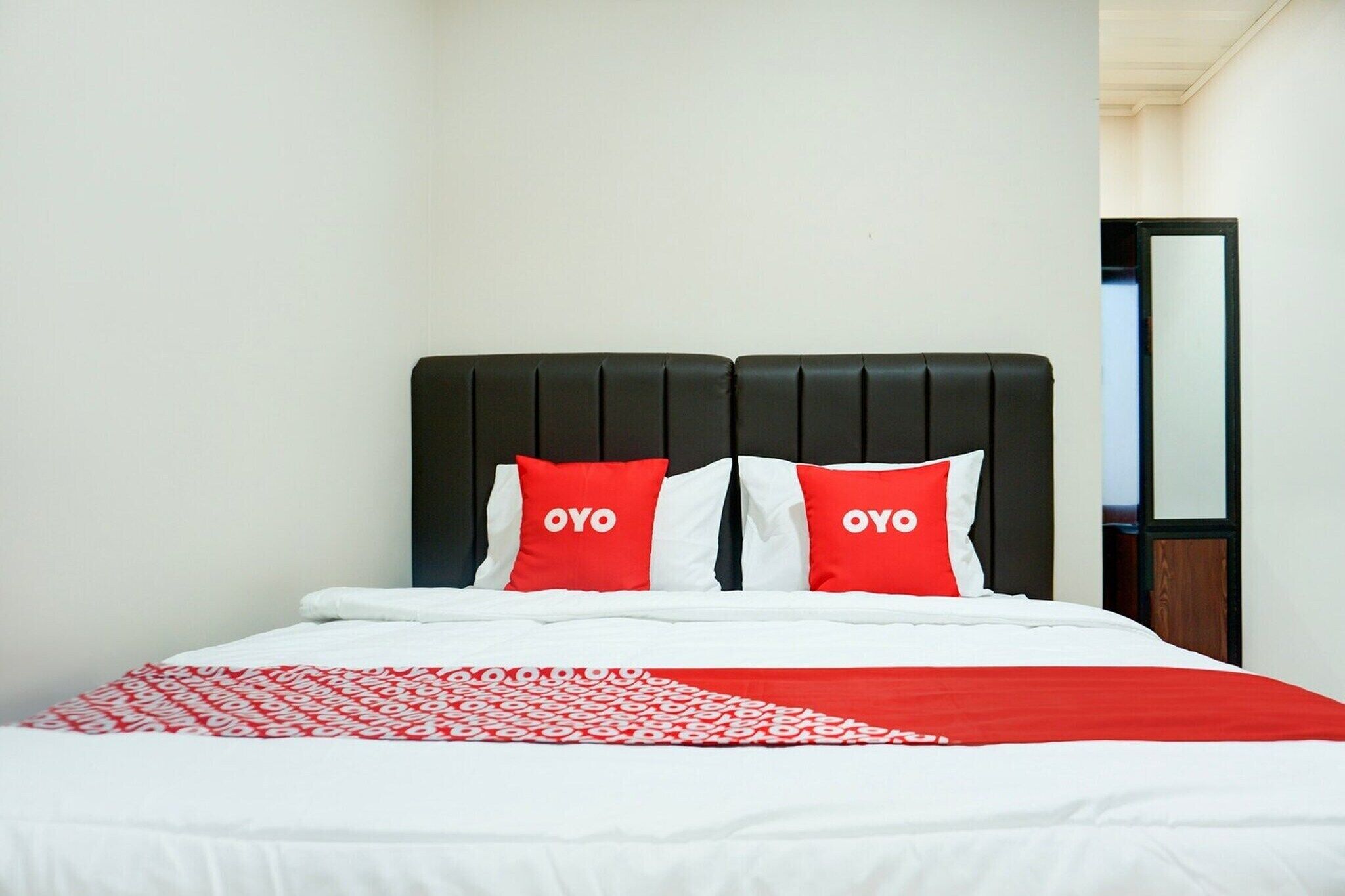 A bed with a black headboard, two pillows with 'OYO' branding, and a red and white patterned blanket.