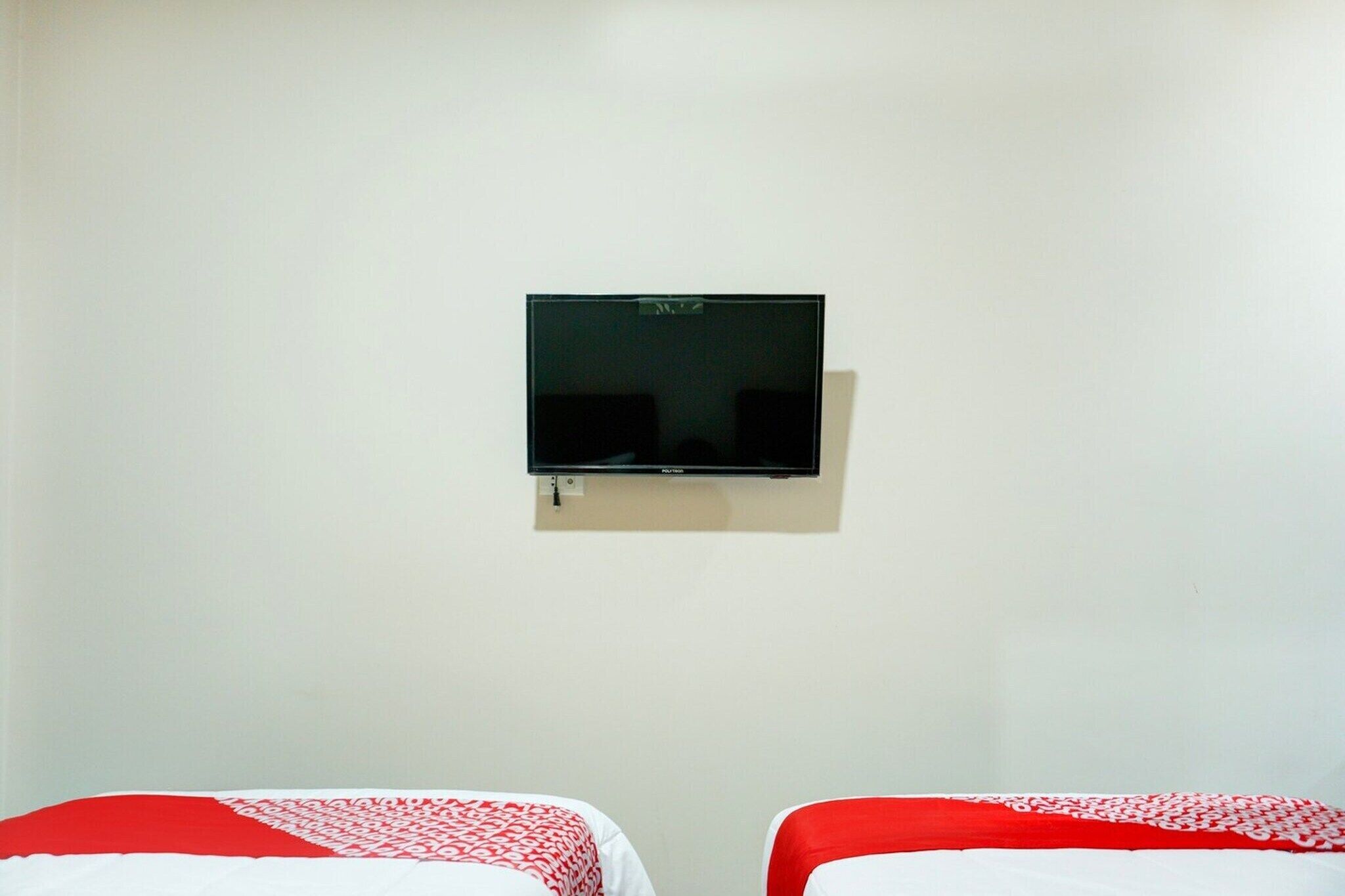 A room with two beds, a wall-mounted TV, and a plain white wall.