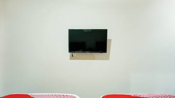 A room with two beds, a wall-mounted TV, and a plain white wall.