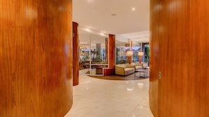En modern hotellobby med träkolonner, en sittgrupp och en glasvägg med växter.